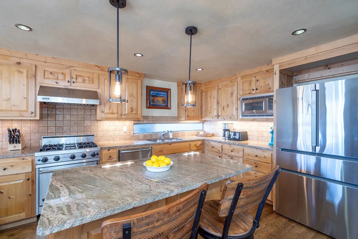 A modern kitchen with granite countertops, stainless steel appliances, wooden cabinetry, and pendant lighting. The layout is open, inviting guests to cook, gather, and socialize.