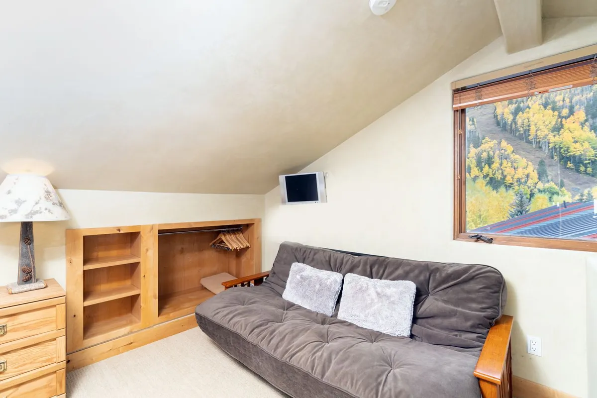 A futon couch next to a window with a scenic view, accompanied by a wooden bedside table. The space feels inviting and adaptable, suitable as an additional sleeping area when needed.