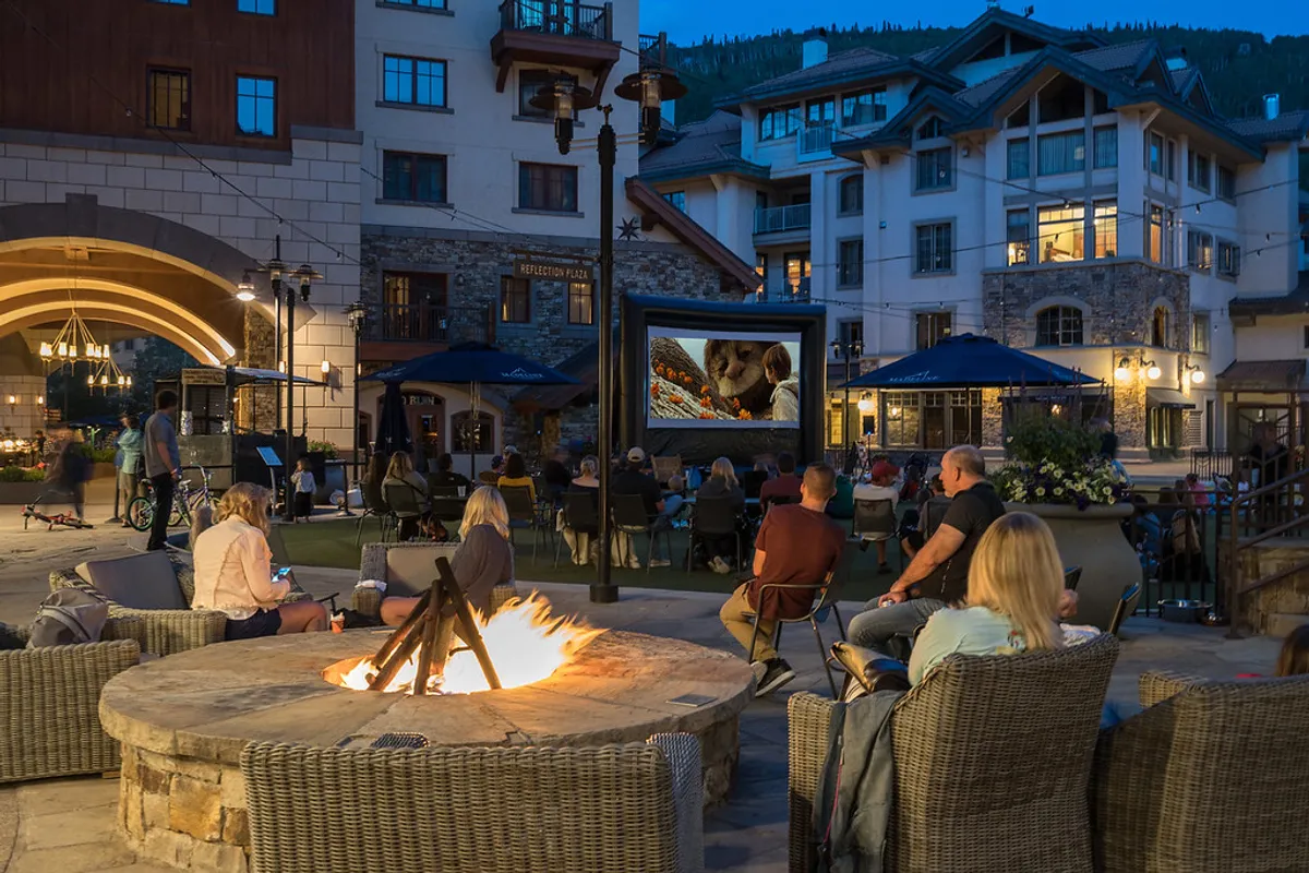 An inviting exterior scene featuring guests gathered around a fire pit, enjoying an outdoor movie under the stars. The firelight and communal atmosphere evoke warmth, relaxation, and memorable shared experiences.
