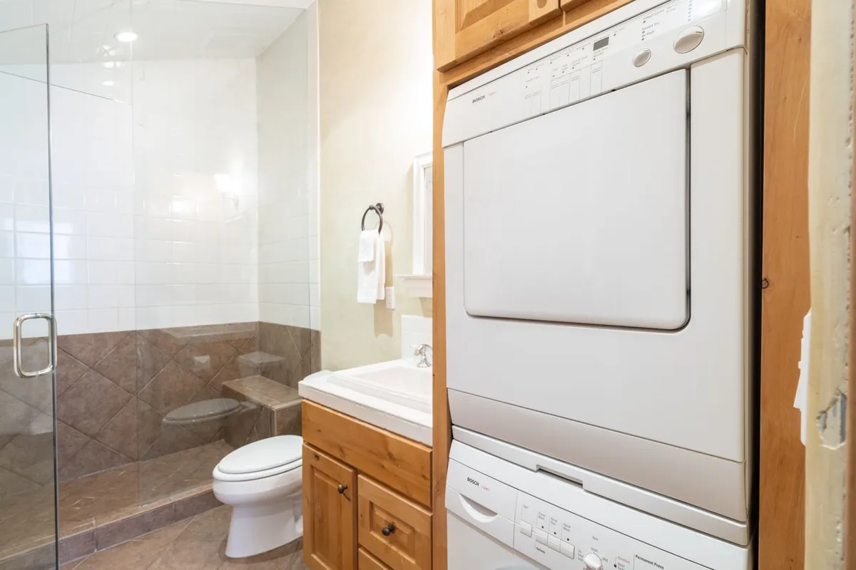 The image features a compact, efficient laundry area with a washing machine and dryer set neatly into wooden cabinetry. The space is tidy, well-lit, and designed for practical use, emphasizing the ease of doing laundry during your stay.