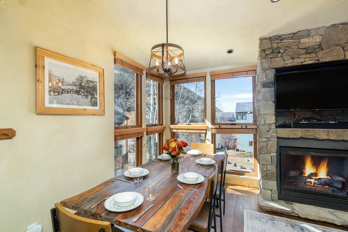 A cozy dining area featuring a prominent dining table, a glowing fireplace, large windows with scenic views, and tasteful decor, ideal for family meals and memorable celebrations.